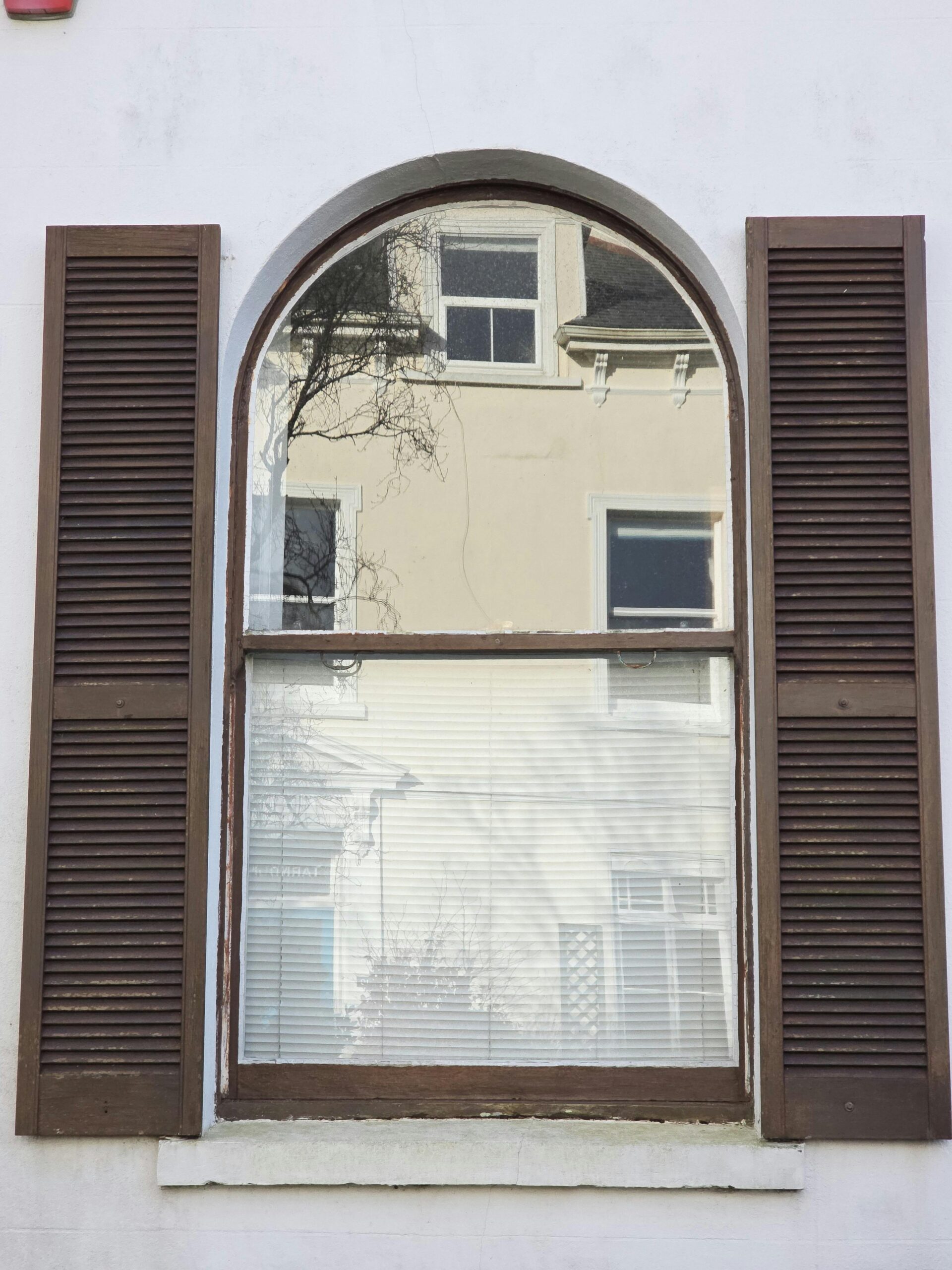 A classic arched window reflecting a neighboring building.